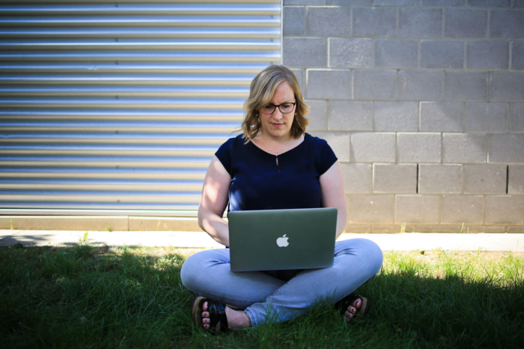 Saskia Baune arbeitet an der Suchmaschinenoptimierung am Laptop, im Schneidersitz auf dem Gras.